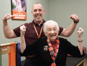 Rehabilitation therapist flexes muscles with smiling senior patient